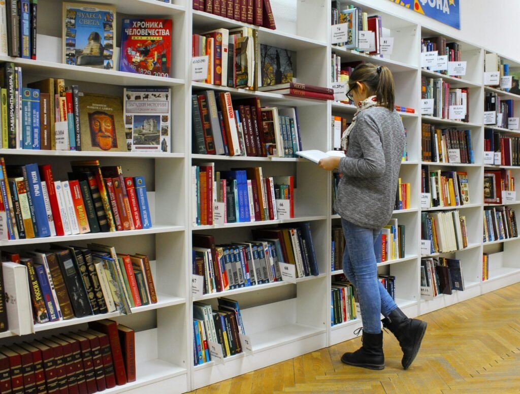 pexels-photo-256455-256455 A young woman stands reading a book in a well-stocked library.